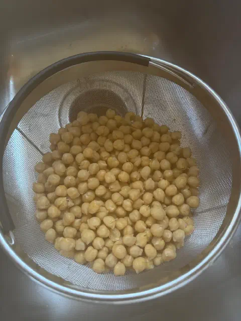 Cooked chickpeas draining in a mesh strainer in the sink