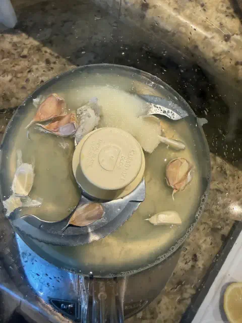 Whole unpeeled garlic cloves and a mound of salt sitting in the lemon juice in the food processor