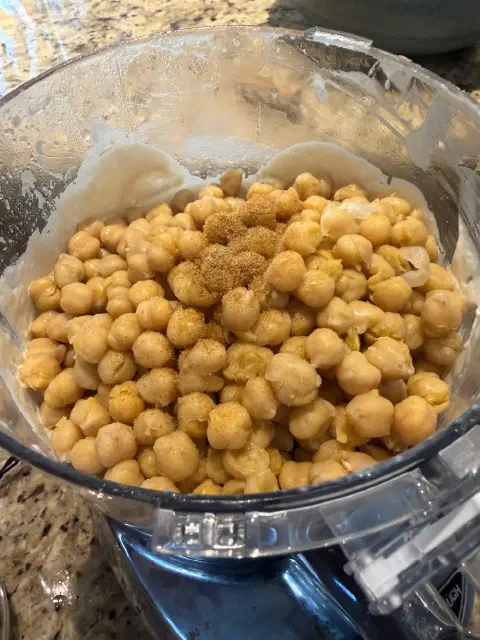 Cooked chickpeas sprinkled with ground cumin on top of the tahini sauce in the food processor