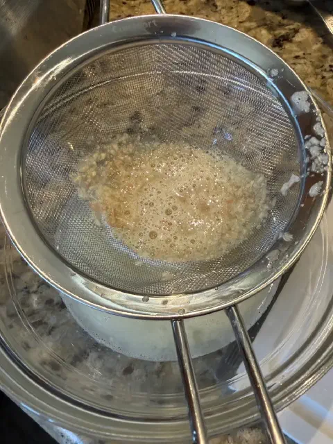 Minced garlic pulp in a fine-mesh strainer over a glass bowl of lemon juice