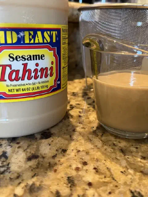 A tub of tahini next to a glass measuring cup filled with tahini